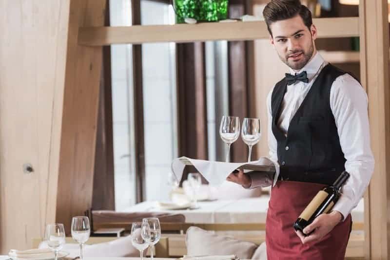 waiter holding wineglasses and bottle